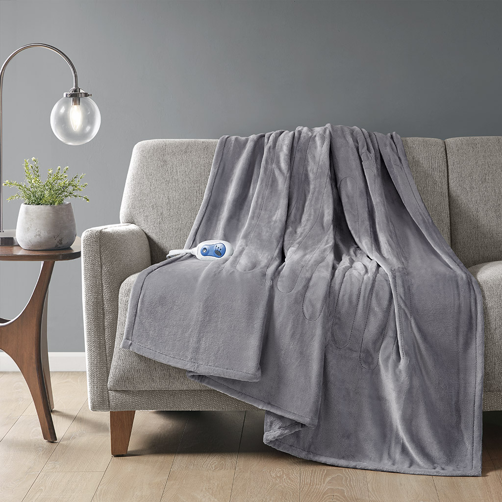 Grey-looking plush Beautyrest heated throw draped over a sofa with one wired hand controller