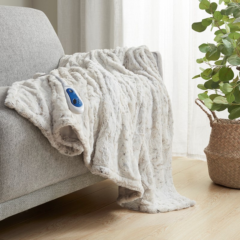 Beautyrest BR54-0911 faux-fur throw shown draped over a sofa with a wired blue controller; exact Snow Leopard variant is not established by this image.