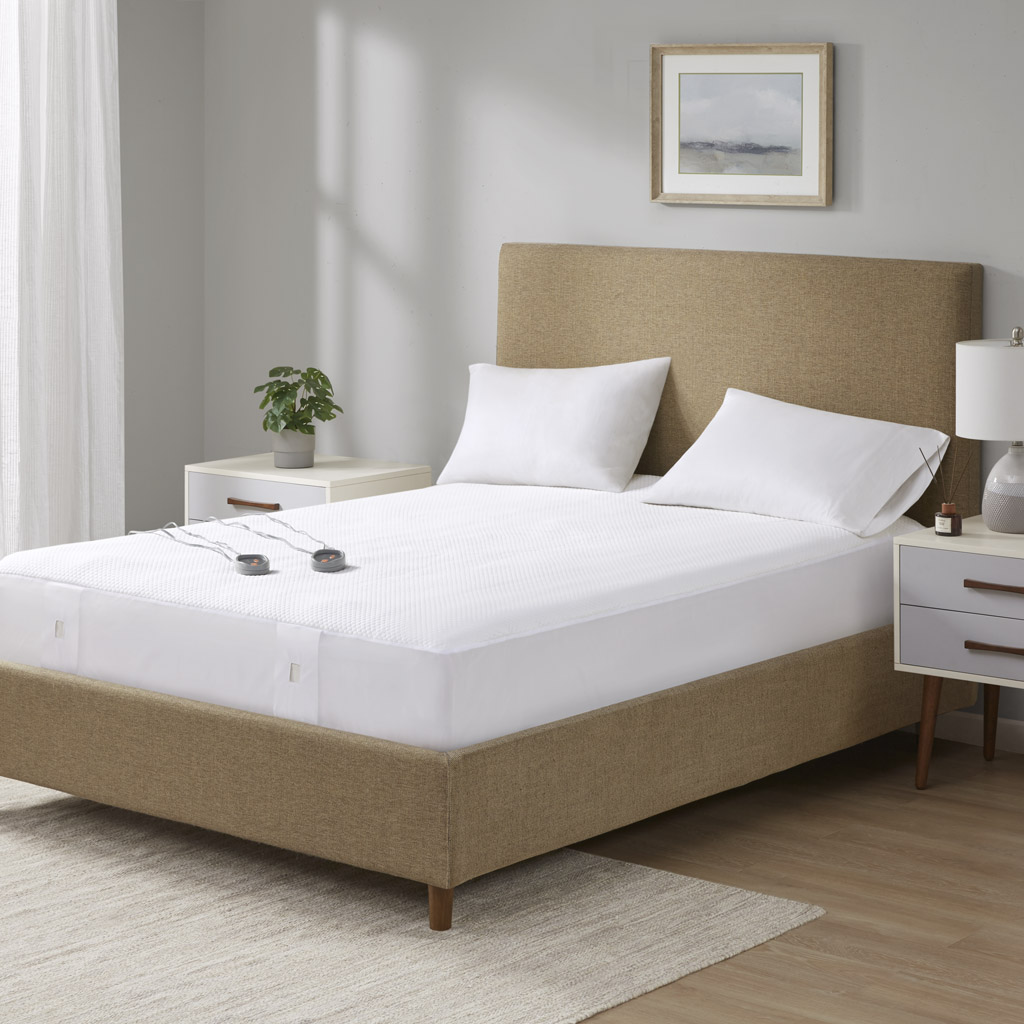 White Beautyrest Cool Touch fitted heated mattress pad on a staged bed, with two wired controllers visible.