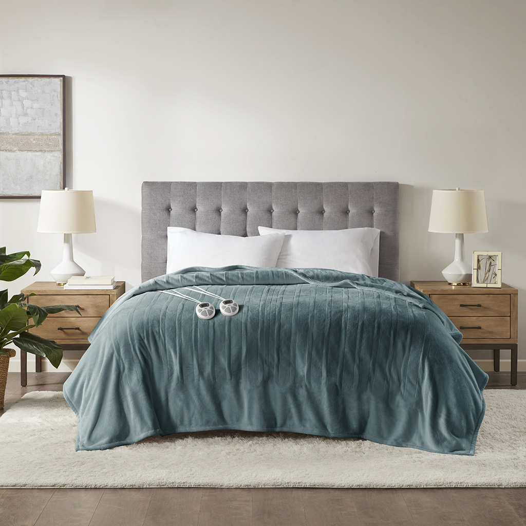 Teal plush Serta heated blanket staged across a bed with control heads