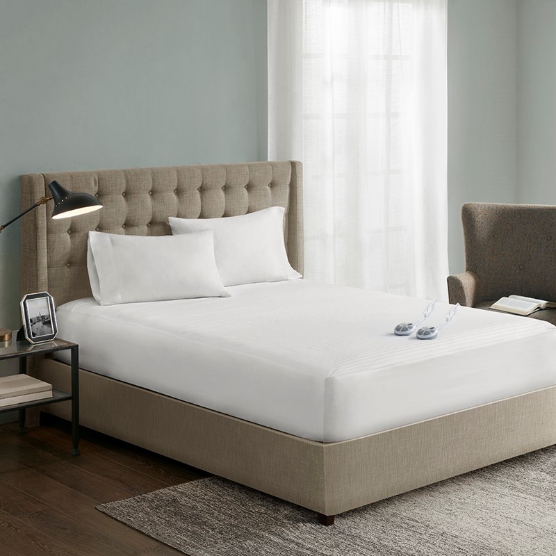 Serta white waterproof heated mattress pad shown on a staged bed with two wired hand controls; shared family image, not size-specific.