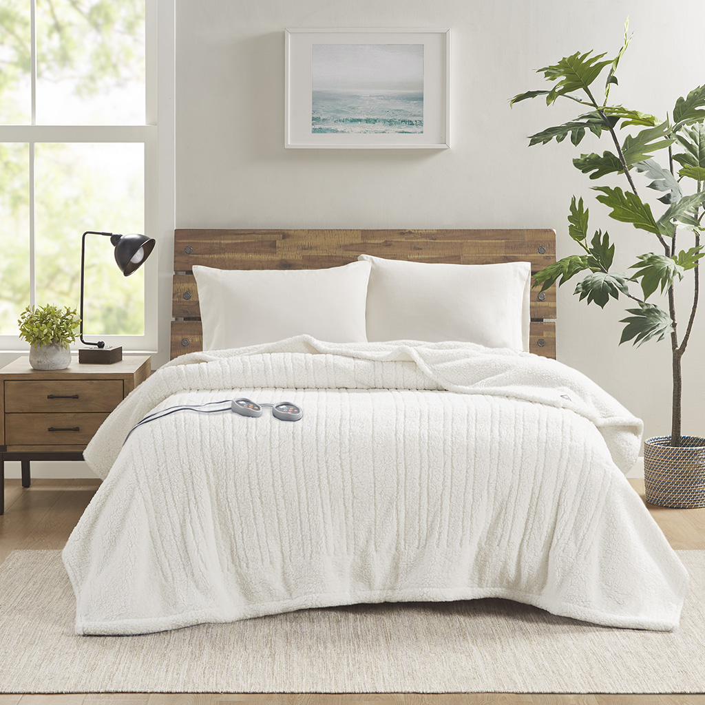 Ivory True North Sherpa heated bed blanket staged on a bed with two controllers