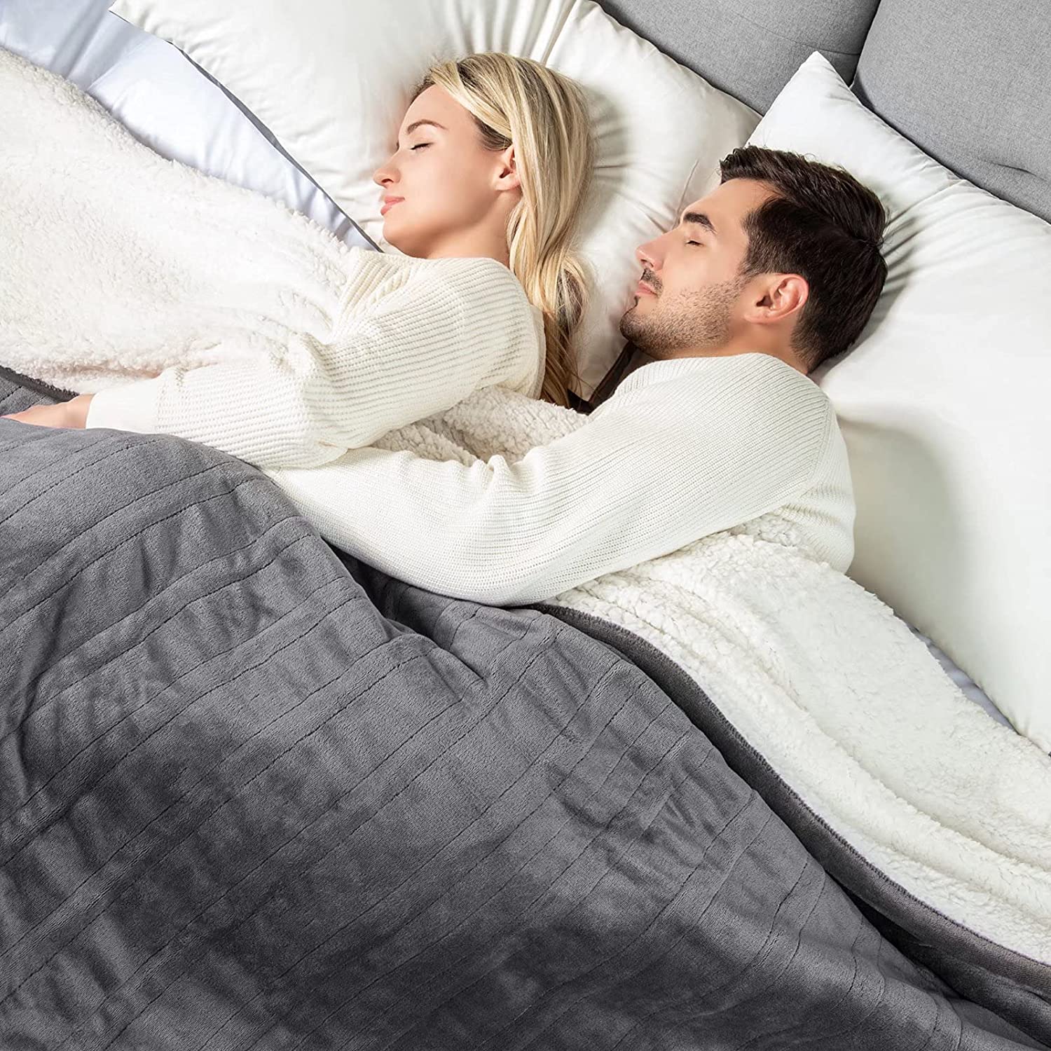 Gray flannel and sherpa blanket shown draped over sleepers on a bed in the WOOMER product-page lifestyle image
